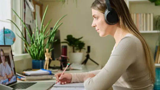 Estudiante con auriculares tomando apuntes durante una clase online
