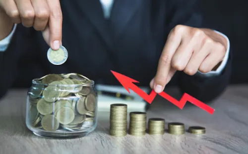 Persona introduciendo una moneda en un frasco junto a pilas de monedas y una flecha descendente