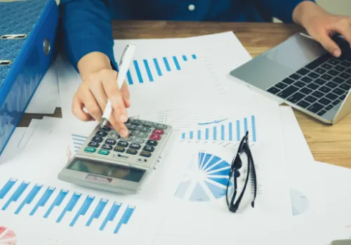Persona analizando gráficos económicos con una calculadora y un ordenador portátil