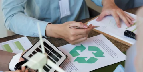 Personas analizando un proyecto de sostenibilidad con símbolos de reciclaje y modelos de energías renovables.
