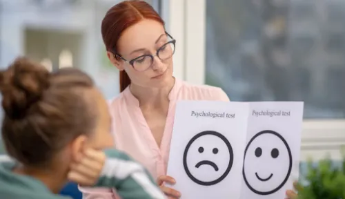 Profesional mostrando a una niña dos tarjetas con una cara triste y otra sonriente