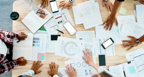 Grupo de personas trabajando alrededor de una mesa con documentos, gráficos, tabletas y teléfonos móviles